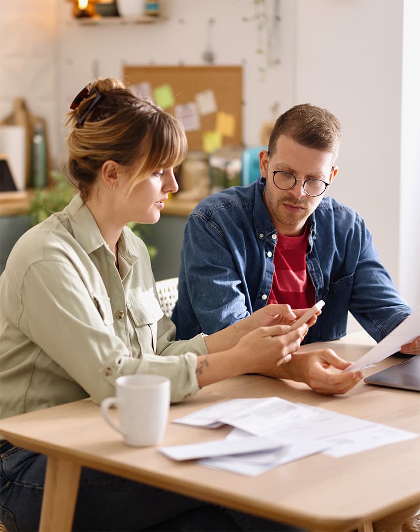 Ein Mann und eine Frau sitzen gemeinsam zuhause am Küchentisch mit einem Laptop und Dokumenten.