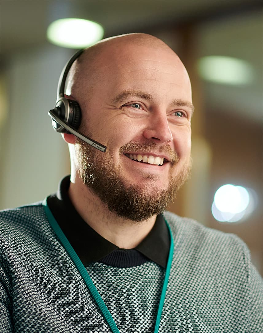 Ein Mann trägt ein Headset und lächelt, während er ein Telefonat führt.